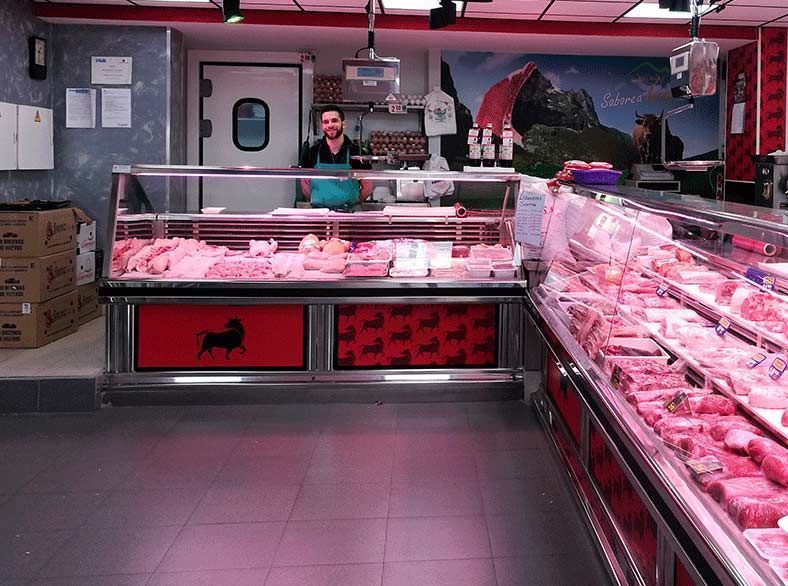 Un hombre está detrás de un mostrador de carne en una carnicería.
