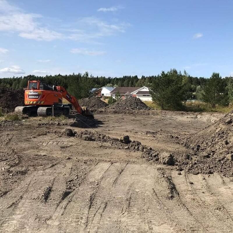 Oranssi kaivinkone tasoittaa maata rakennustyömaalla sinisen taivaan alla.