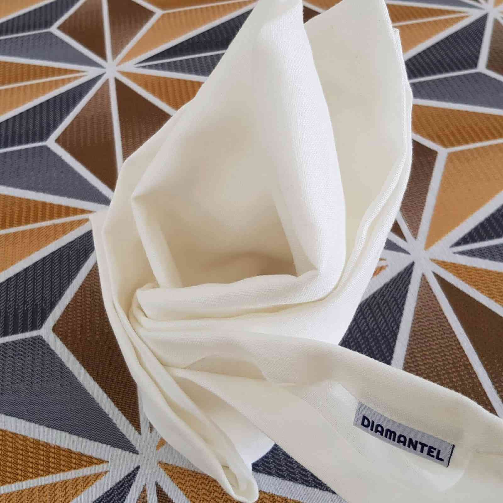 Una servilleta de tela color crema doblada en forma decorativa, sobre una mesa con un estampado geométrico marrón y blanco.