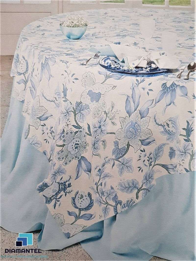 Una mesa redonda cubierta con un mantel azul pálido y sobre ella un mantel con estampado floral blanco y azul.