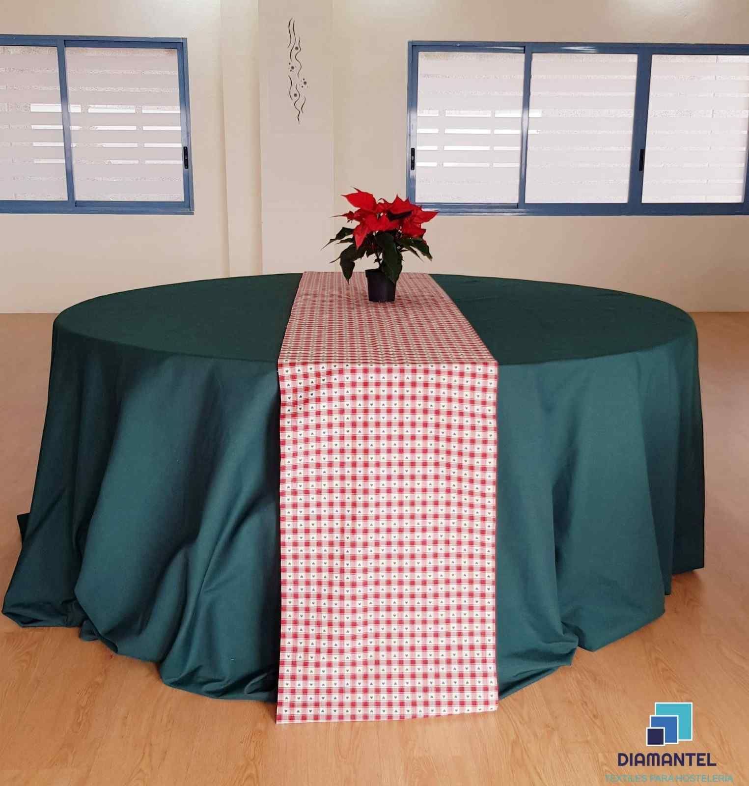 Una mesa redonda con un mantel verde oscuro, un camino de mesa estampado