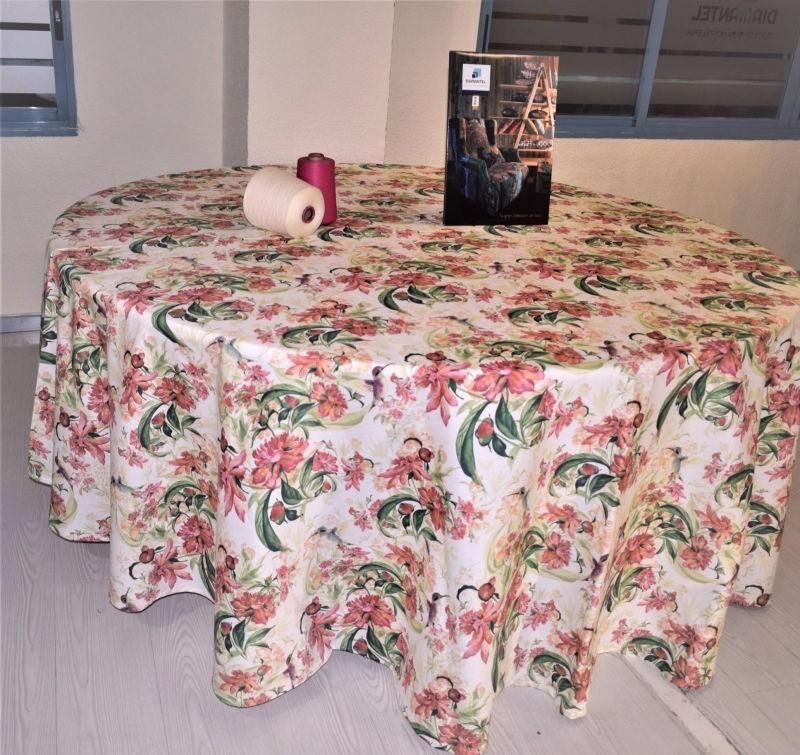 Una mesa redonda cubierta con un mantel color crema con un estampado floral rosa y verde, que incluye una bobina y una caja.