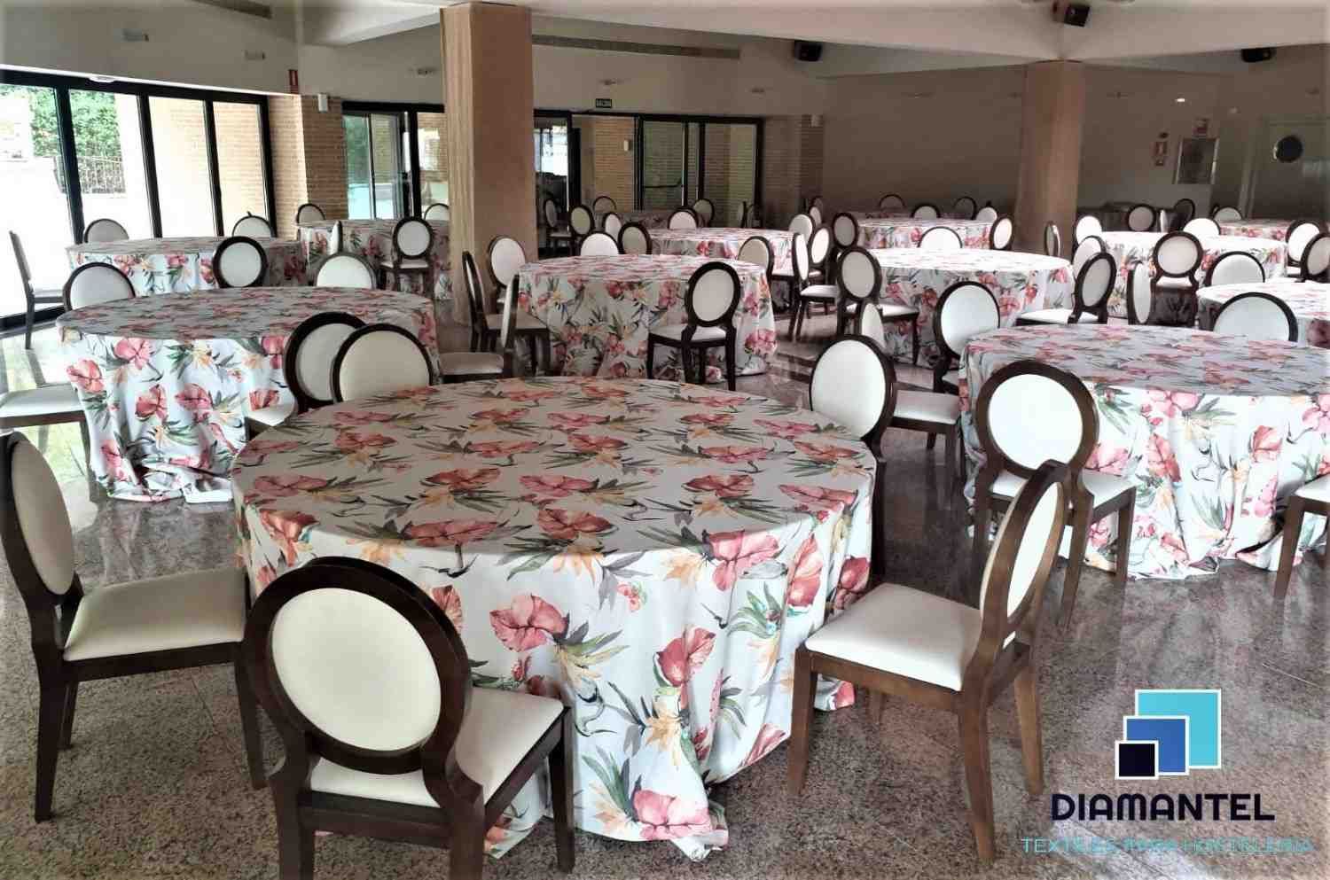 Un salón de eventos repleto de mesas redondas cubiertas con manteles blancos con estampados florales rosas y sillas a juego.