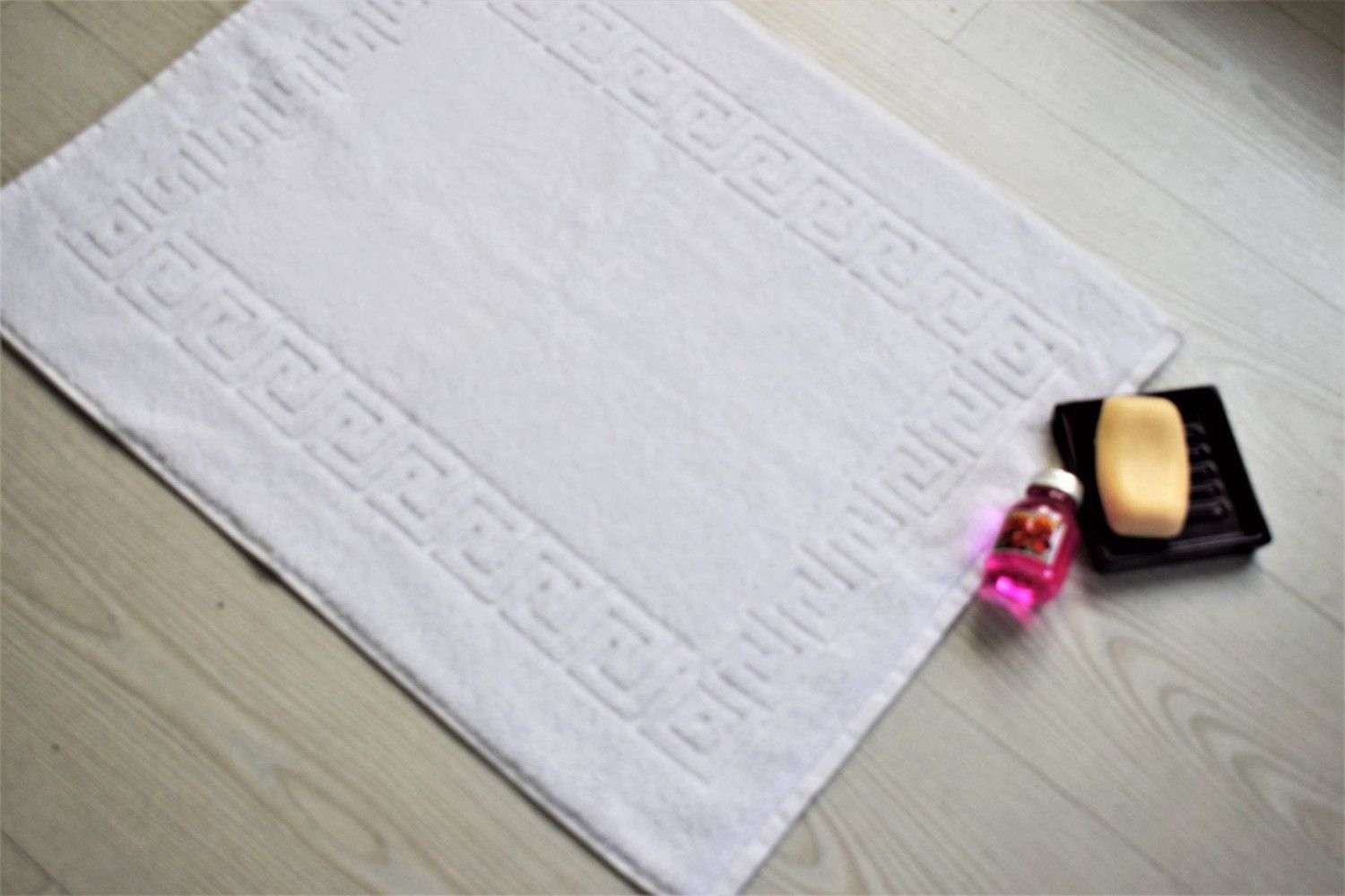 Una alfombrilla de baño blanca con un borde de greca griega yace sobre un suelo de madera clara
