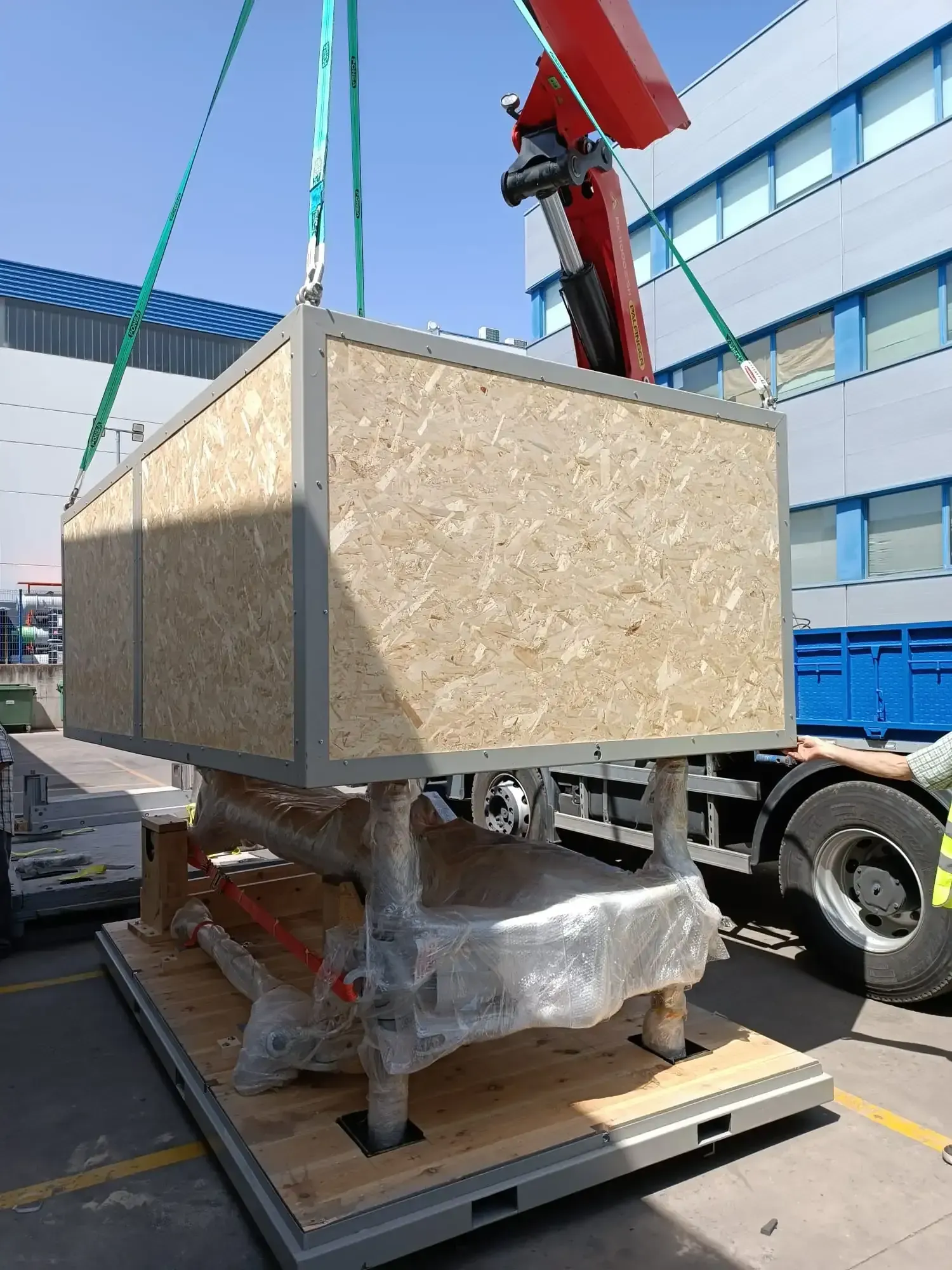 Una gran caja de madera suspendida por una grúa sobre la plataforma de un camión.