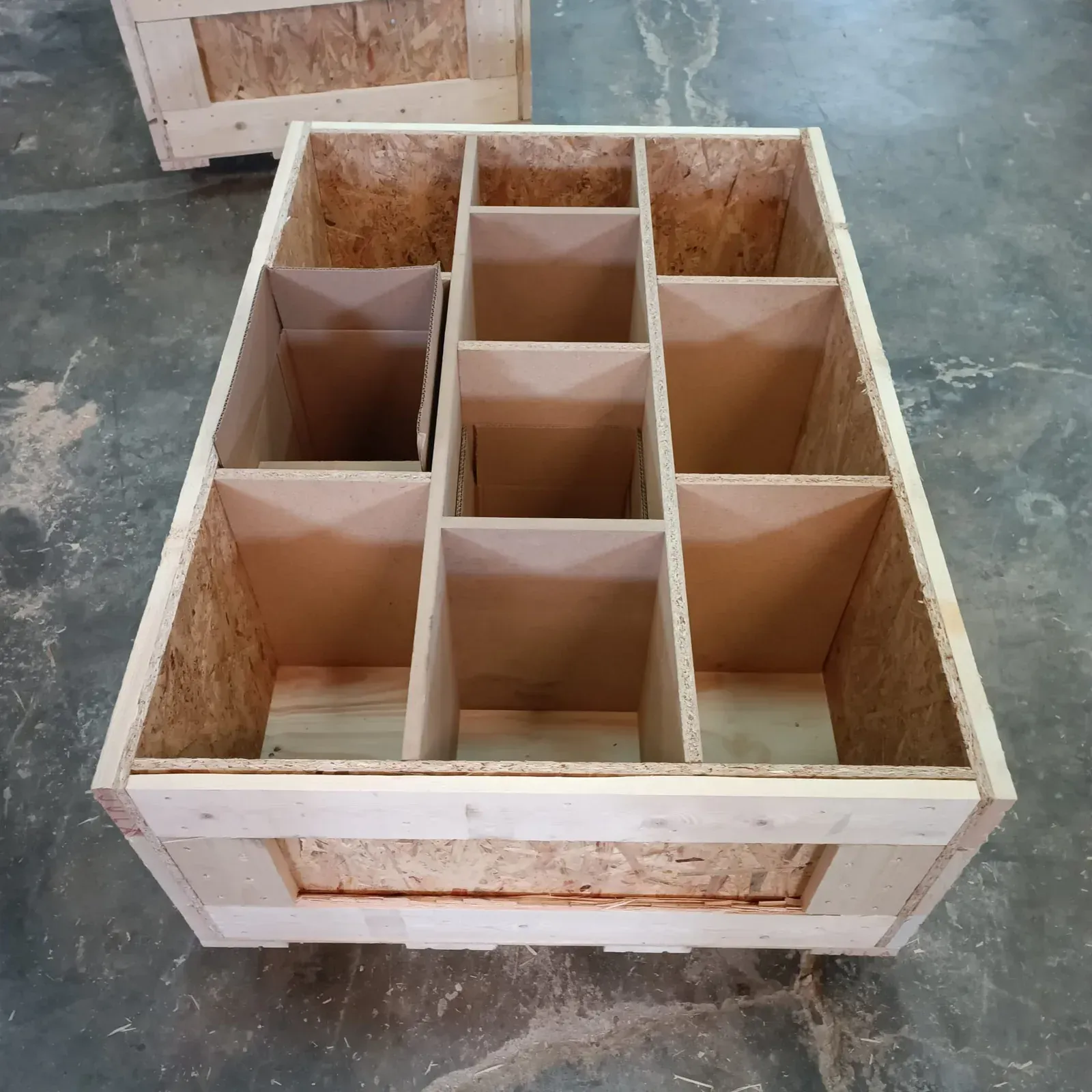 Caja de madera con divisores interiores, vista desde arriba, sobre un piso de concreto.