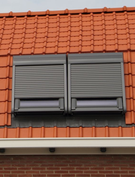 Deux volets gris sur un toit de tuiles orange, avec un petit auvent blanc en dessous.