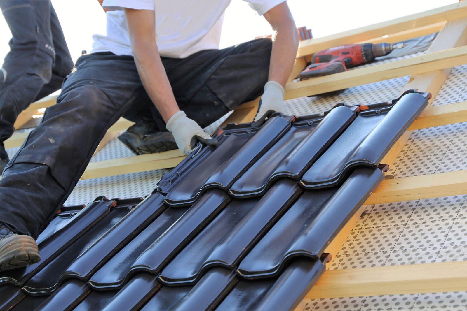 Un couvreur pose des tuiles noires sur une toiture