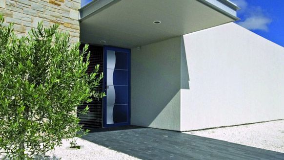 L'entrée d'une maison moderne, avec une porte d'entrée bleu foncé, un mur à l'aspect pierre, un petit arbre et une allée en pierre sombre.