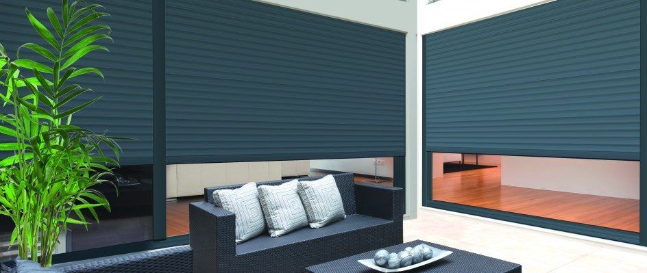 Volets roulants extérieurs modernes gris foncé installés sur de grandes fenêtres d'une terrasse avec mobilier de jardin et plante en pot.