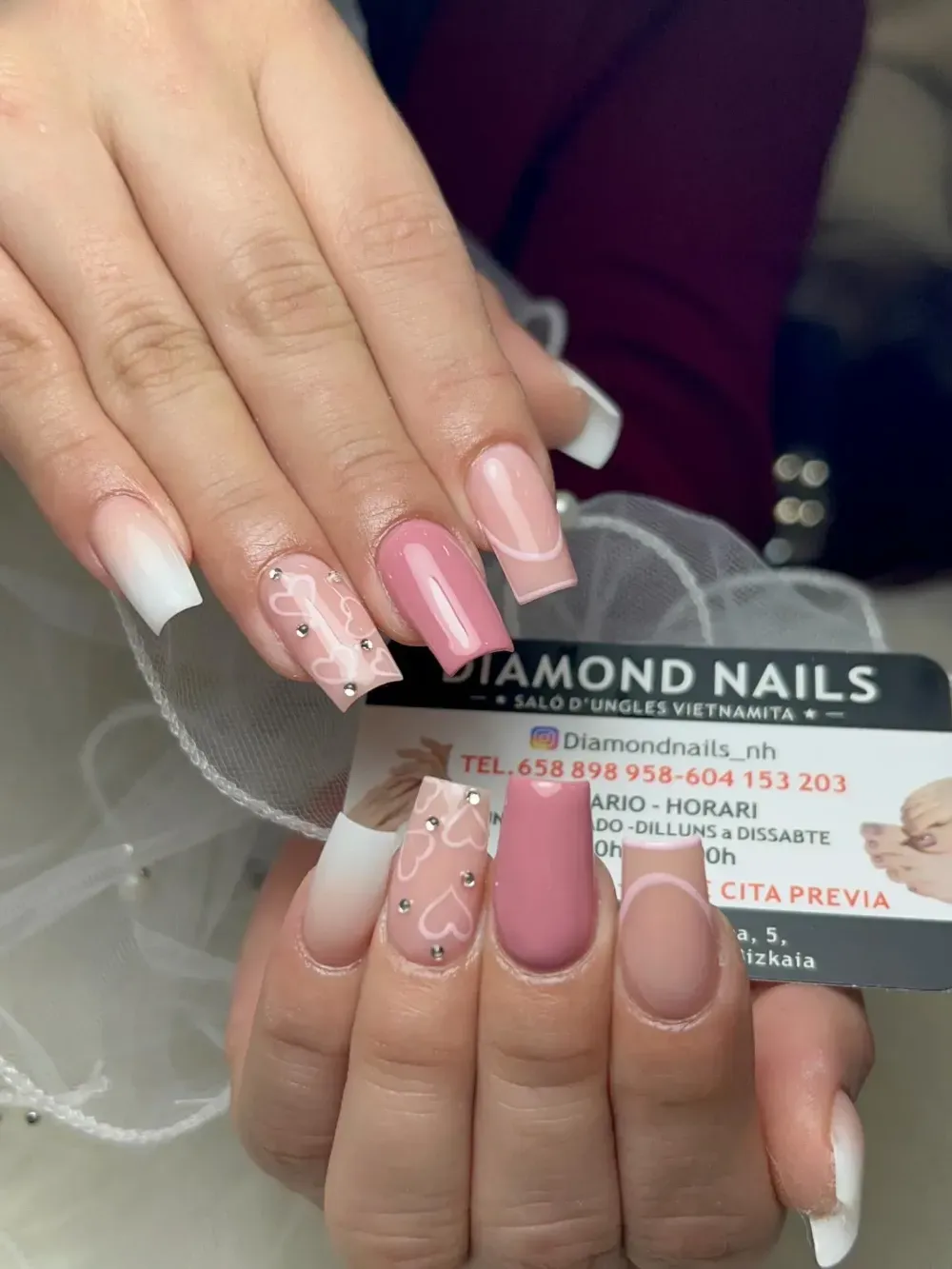 Manos con manicura francesa rosa nude y decoración floral sosteniendo una tarjeta de Diamond Nails.