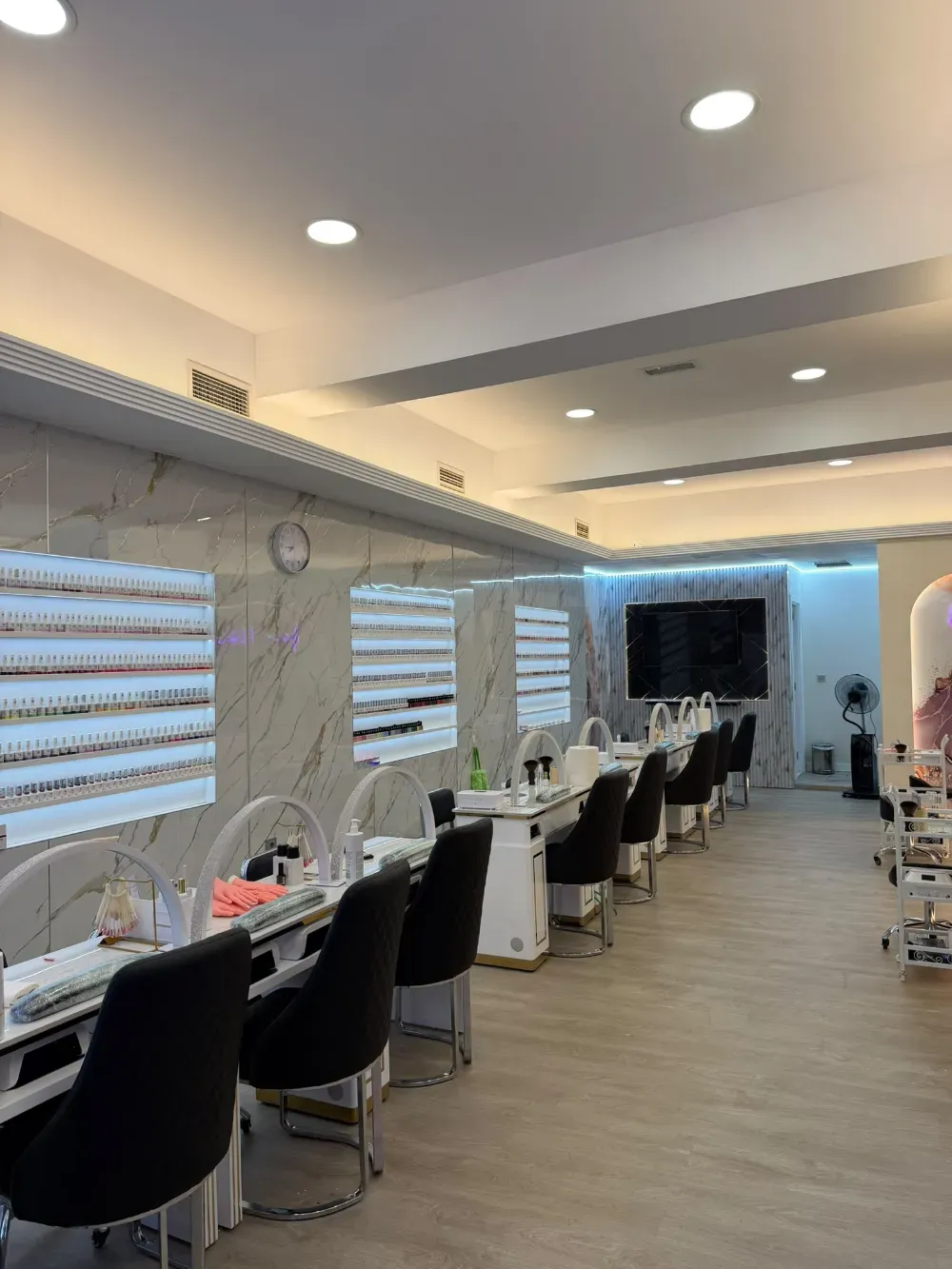 Salón de maquillaje moderno con espejos, sillas negras, tocadores blancos y una iluminación suave en el techo