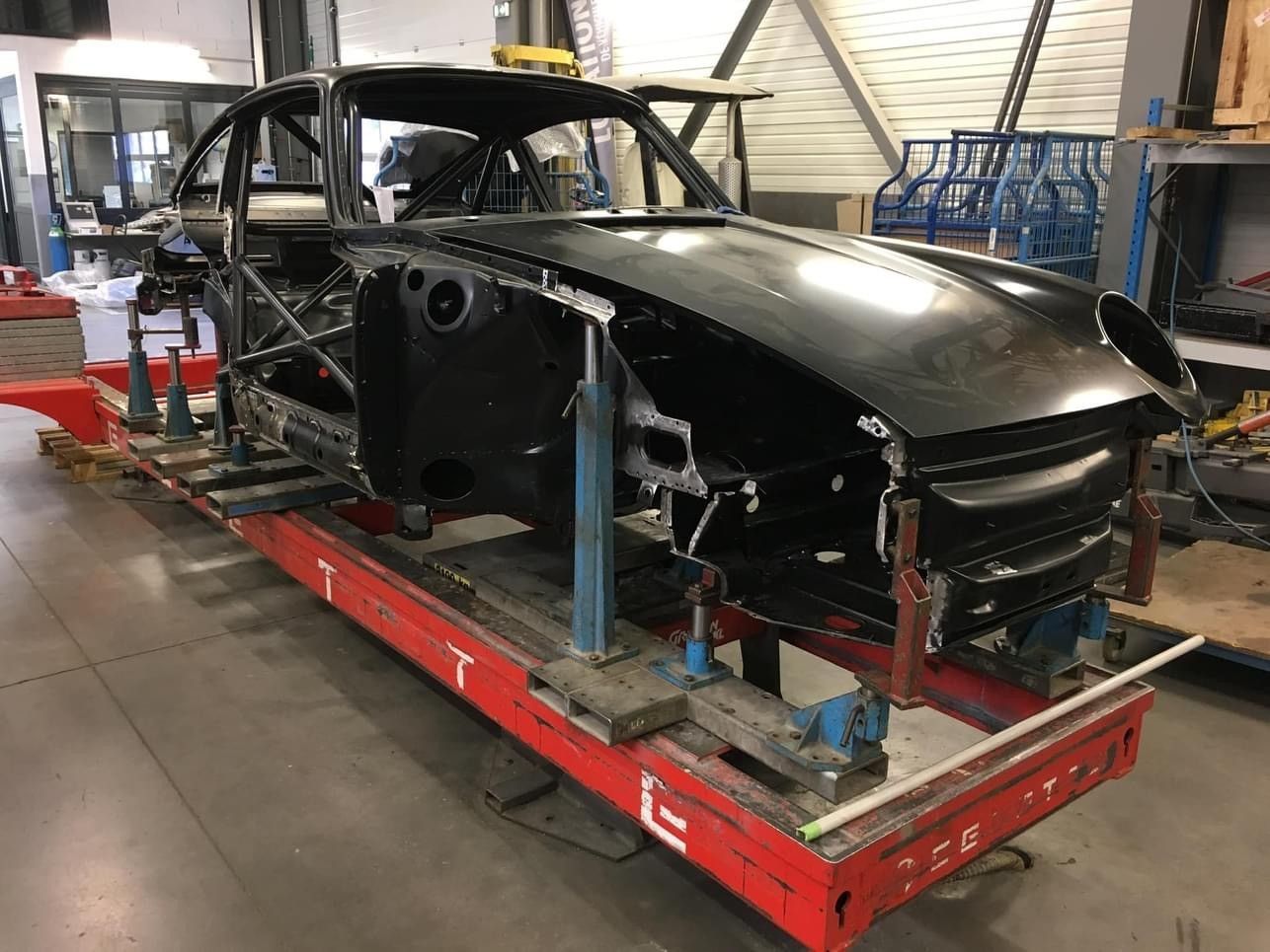 Carrosserie de voiture classique noire sur châssis rouge, à l'intérieur d'un atelier.