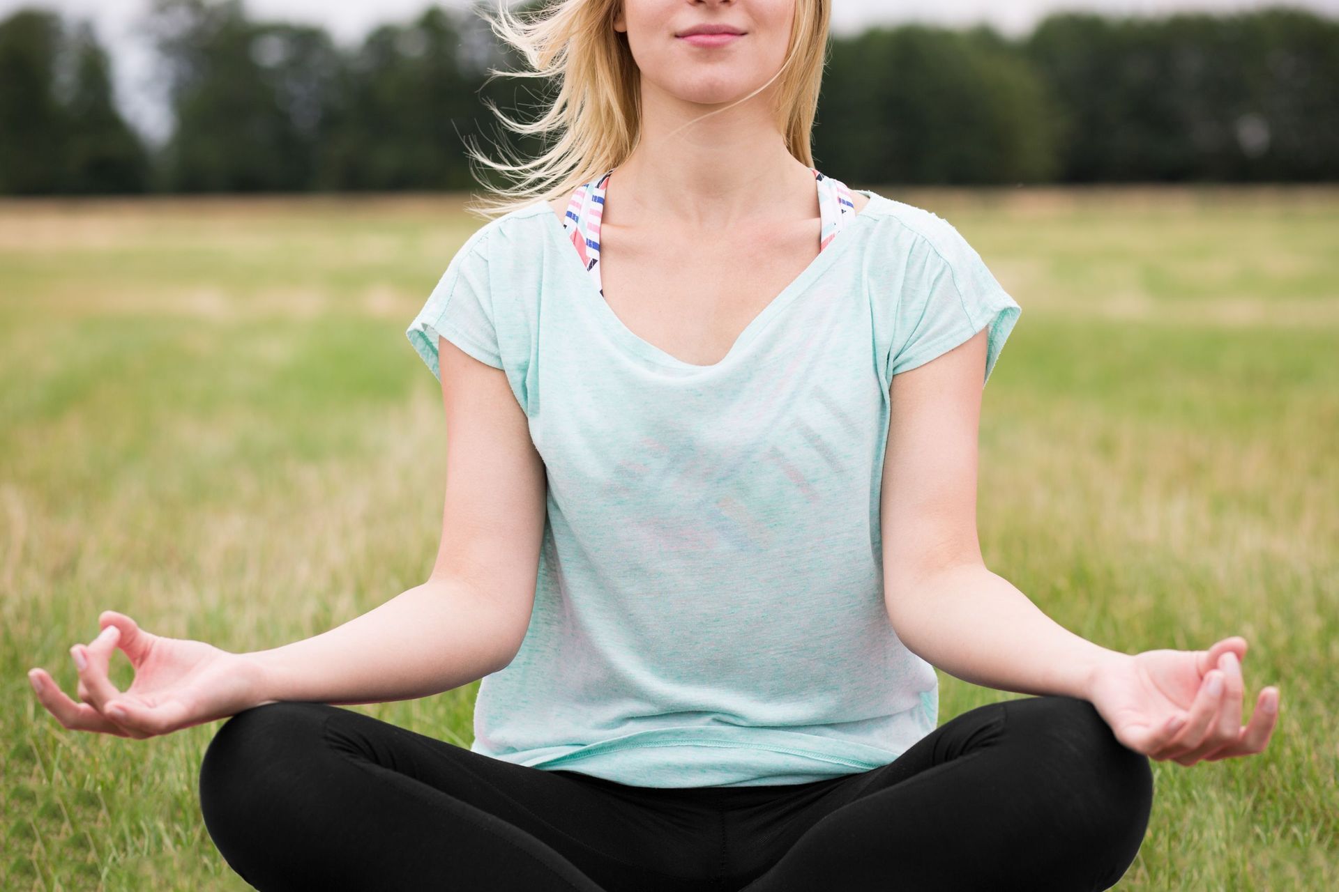 Eine Frau sitzt im Lotussitz auf einem Feld.