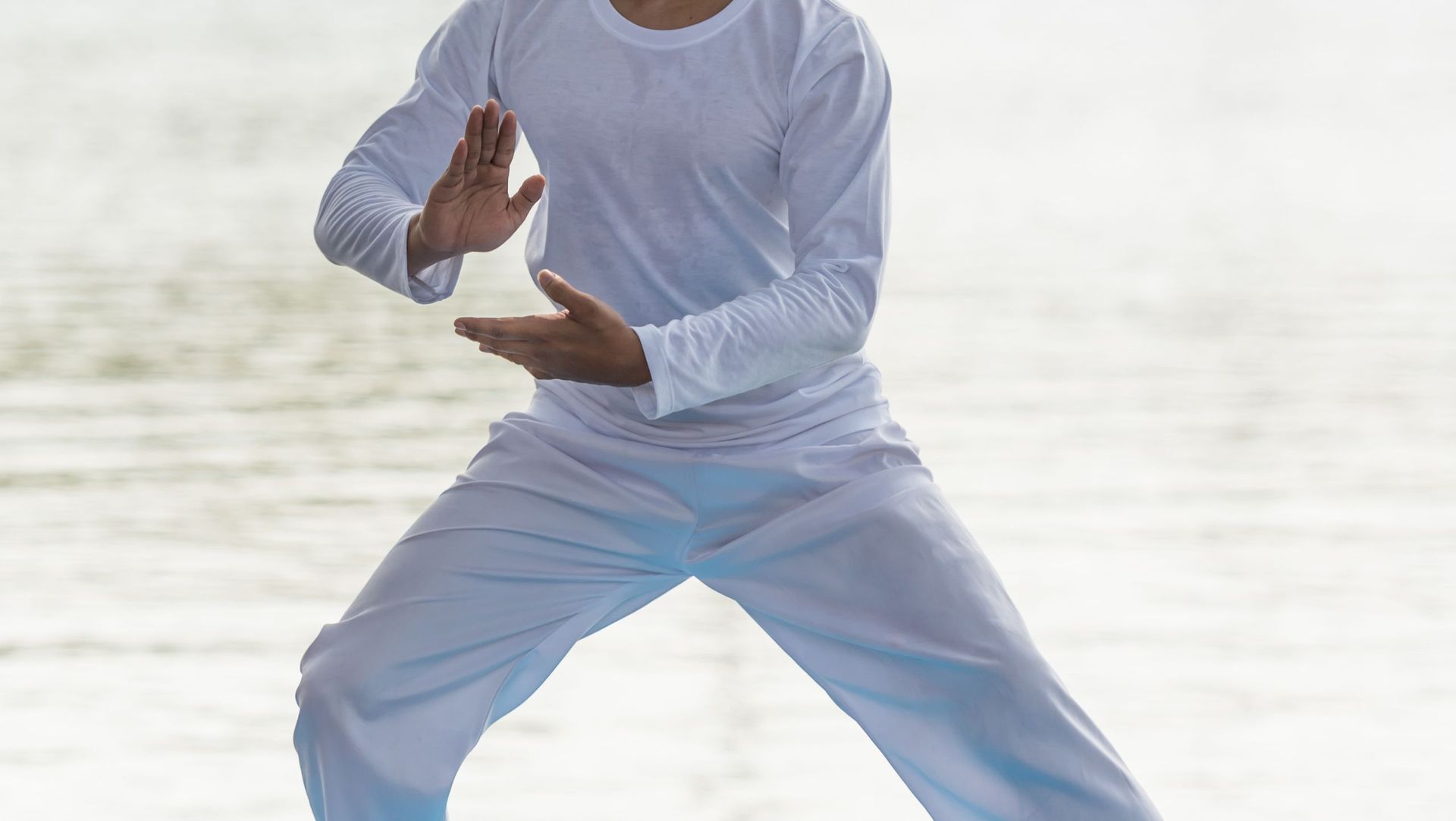 Ein Mann in einem weißen Hemd und blauen Hosen übt am Strand Kampfsport.