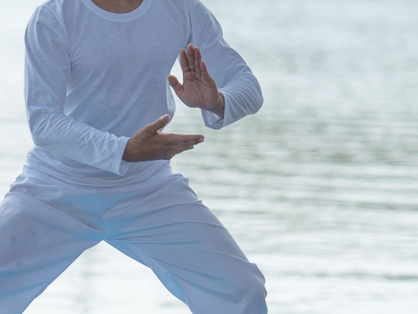 Ein Mann in einem weißen Hemd und weißen Hosen übt am Strand Kampfsport.