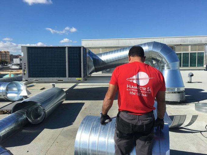 Un técnico con camisa roja inspecciona una unidad eléctrica Mitsubishi en la azotea bajo el cielo azul.