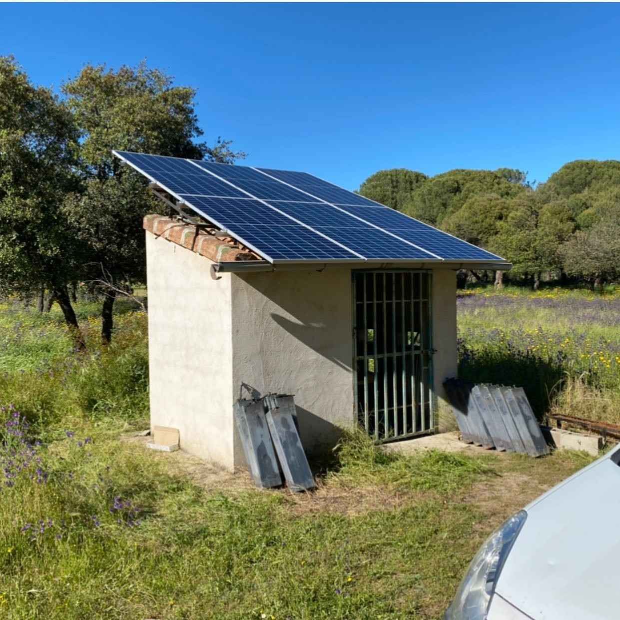 Un pequeño cobertizo de hormigón con paneles solares en un campo de hierba bajo un cielo azul despejado.