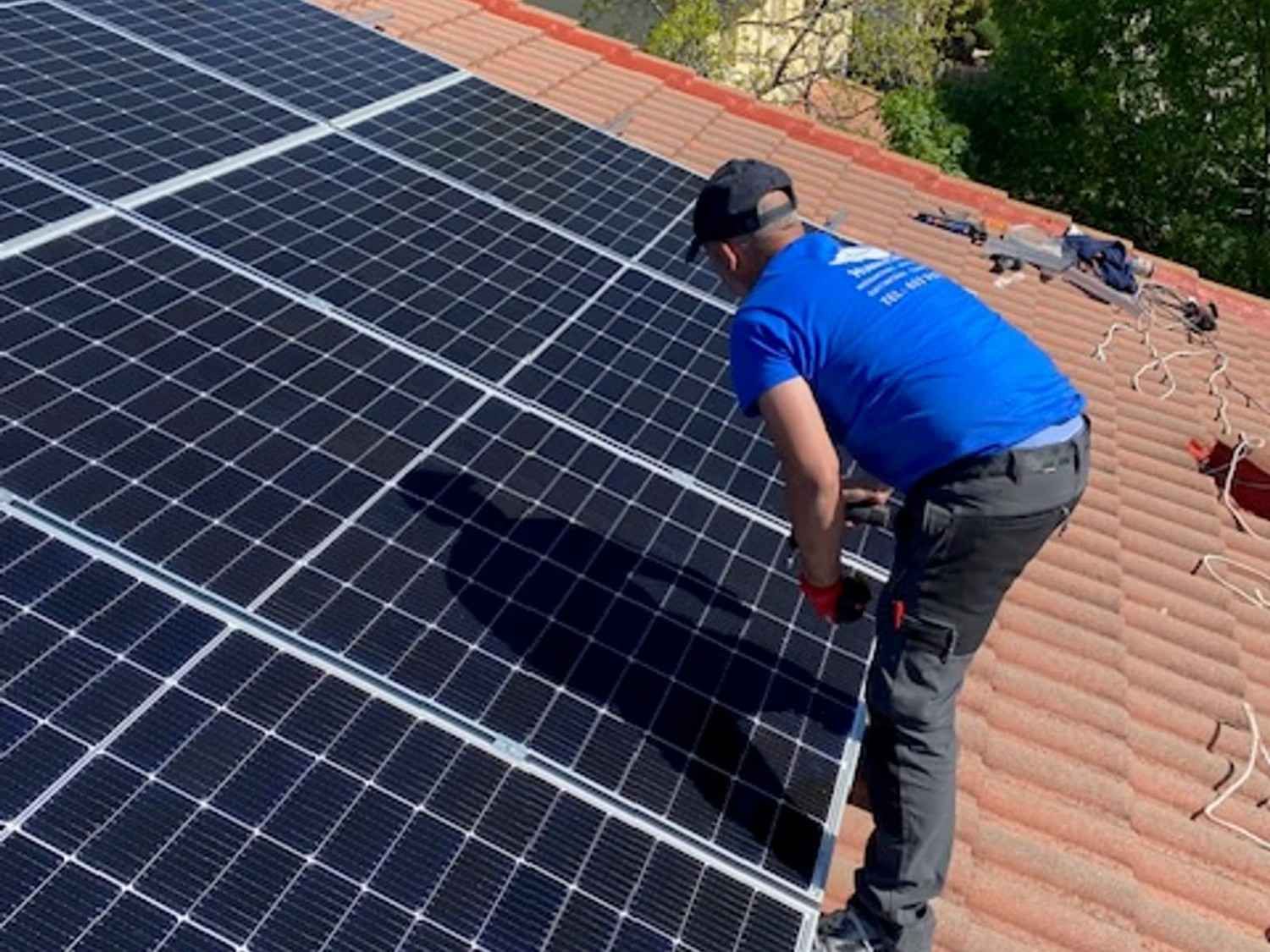 Un trabajador instala paneles solares en un tejado de tejas con una herramienta en la mano.