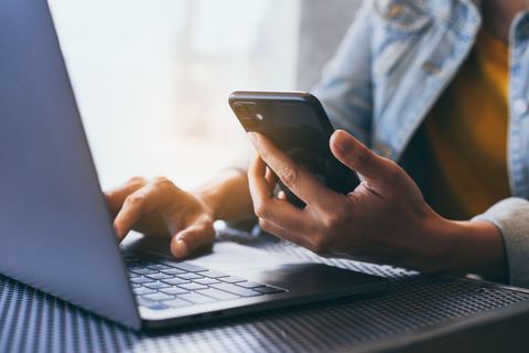 Des mains tapant sur un ordinateur portable tout en tenant un smartphone à un bureau.