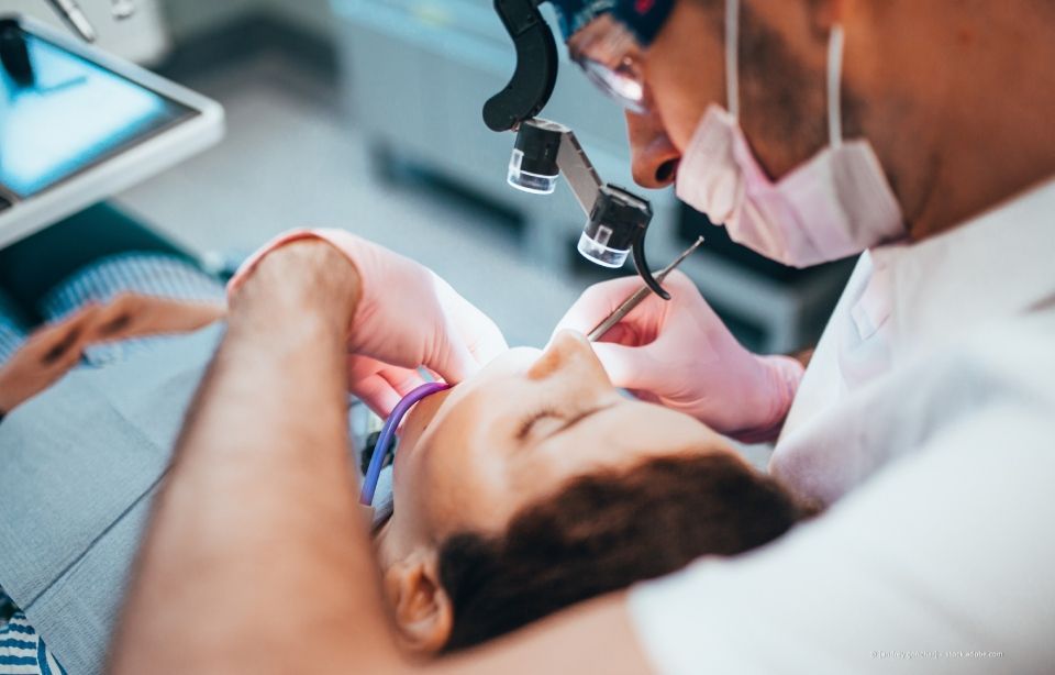 Ein Zahnarzt untersucht in einer Klinik den Mund eines Patienten mit einem Vergrößerungsinstrument.