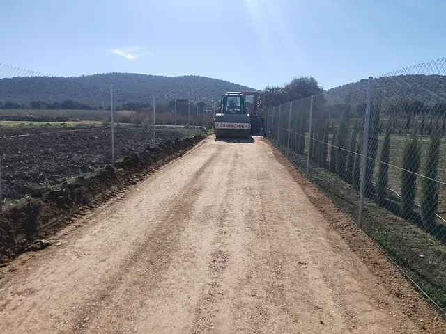 Una excavadora avanza por un camino de tierra al lado de una valla.