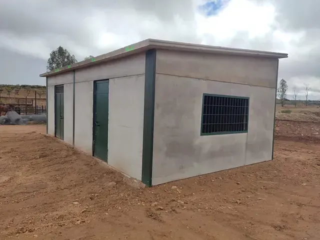 Un pequeño edificio de hormigón con una ventana en medio de un campo de tierra.