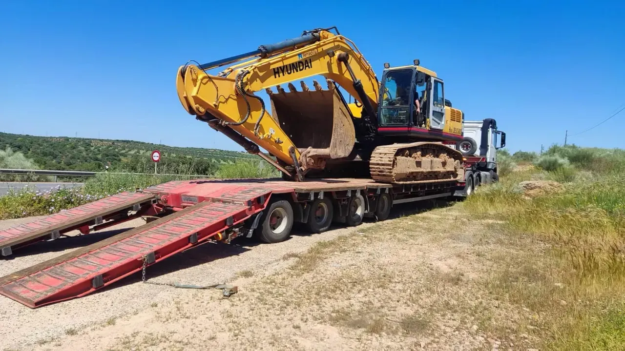 Una excavadora amarilla está sentada encima de un remolque rojo.