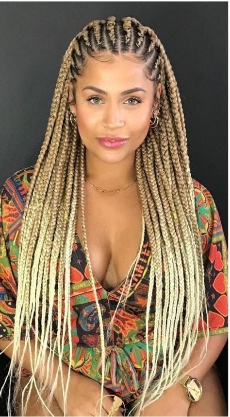 Mujer con largas trenzas rubias y una blusa colorida estampada sobre un fondo negro.