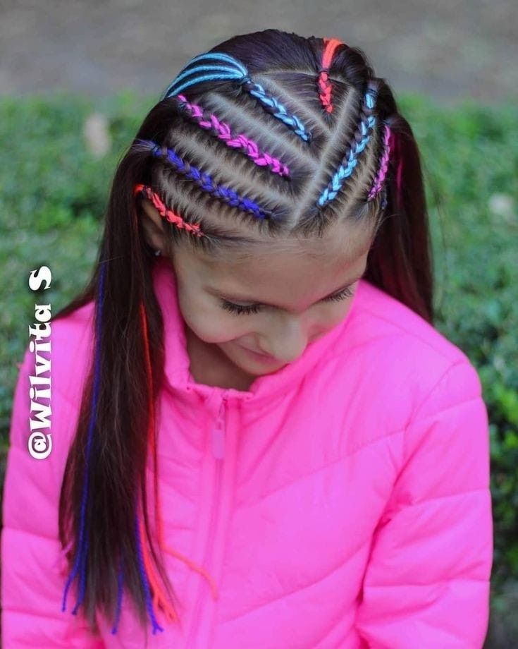 Niña con el pelo trenzado y chaqueta rosa brillante mirando hacia abajo al aire libre.