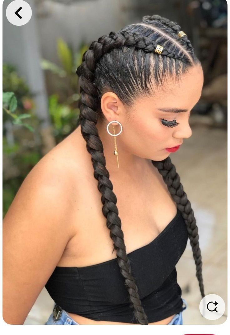 Mujer con el pelo largo trenzado, vestida con una blusa negra y pendientes de aro, mirando hacia abajo al aire libre.