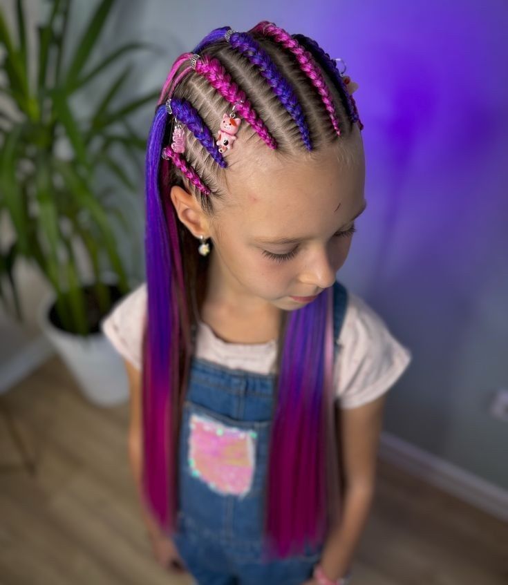 Niña con el pelo trenzado de color rosa y morado, mirando hacia abajo, vestida con un mono vaquero