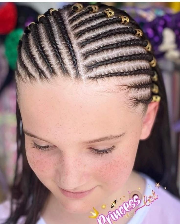 Primer plano de una persona con trenzas africanas decoradas con cuentas doradas, mirando hacia abajo.
