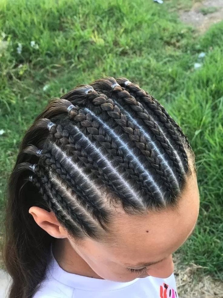 Primer plano de trenzas africanas en una cabeza, con hierba verde al fondo.