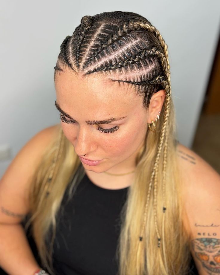 Mujer con intrincadas trenzas africanas y cabello rubio, mirando hacia abajo con una blusa negra.