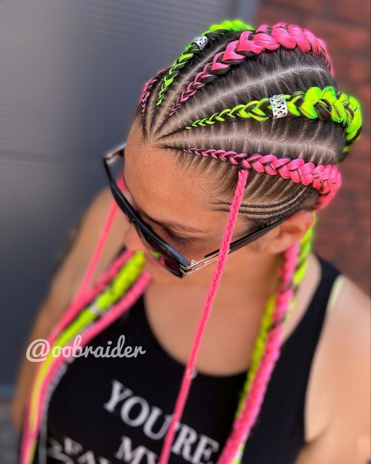 Cabello trenzado con extensiones rosas y verde neón, visto desde arriba, persona con gafas y blusa negra.