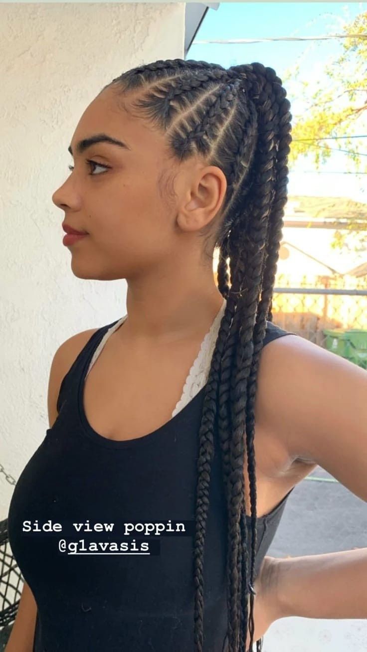 Retrato de perfil de una persona con trenzas largas y una camiseta sin mangas negra, al aire libre cerca de una valla.