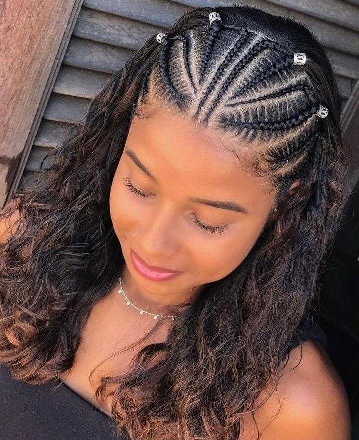 Mujer con cabello largo y ondulado y detalles de trenzas en el cuero cabelludo, mirando hacia abajo con una leve sonrisa.