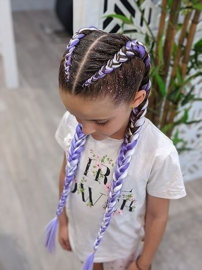 Niña con el pelo trenzado de color morado, mirando hacia abajo, vestida con una camiseta blanca
