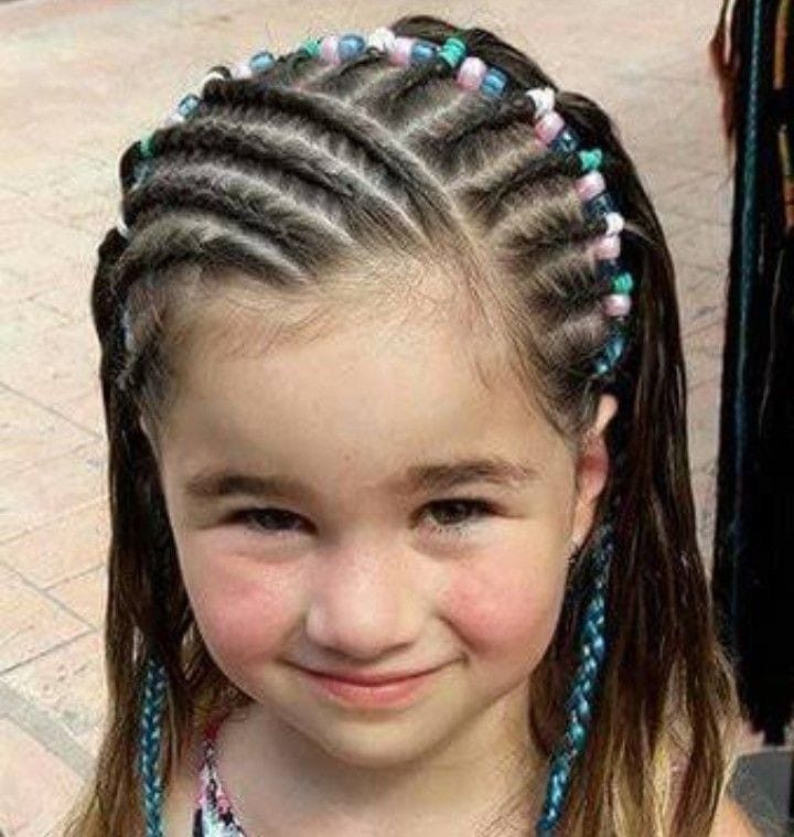 Niña sonriente con el pelo trenzado y cuentas de colores, mirando a la cámara.