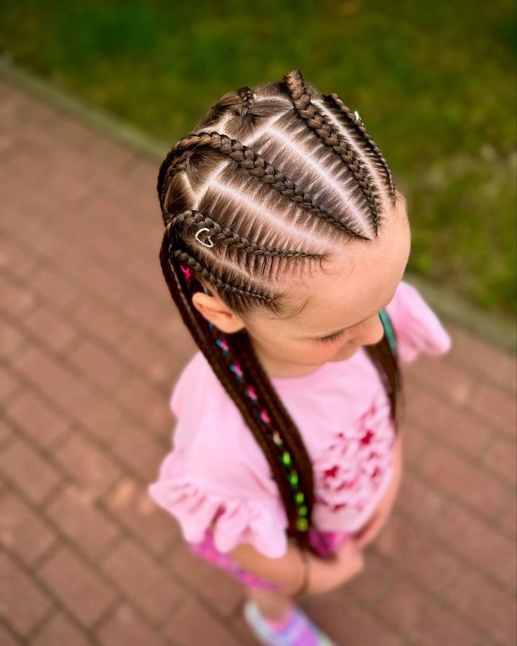 Niña con trenzas africanas y un atuendo rosa, de pie en un sendero de ladrillos al aire libre.