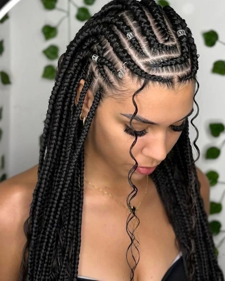 Mujer con peinado de trenzas largas y mechones rizados que enmarcan el rostro, mirando hacia abajo contra un fondo frondoso.