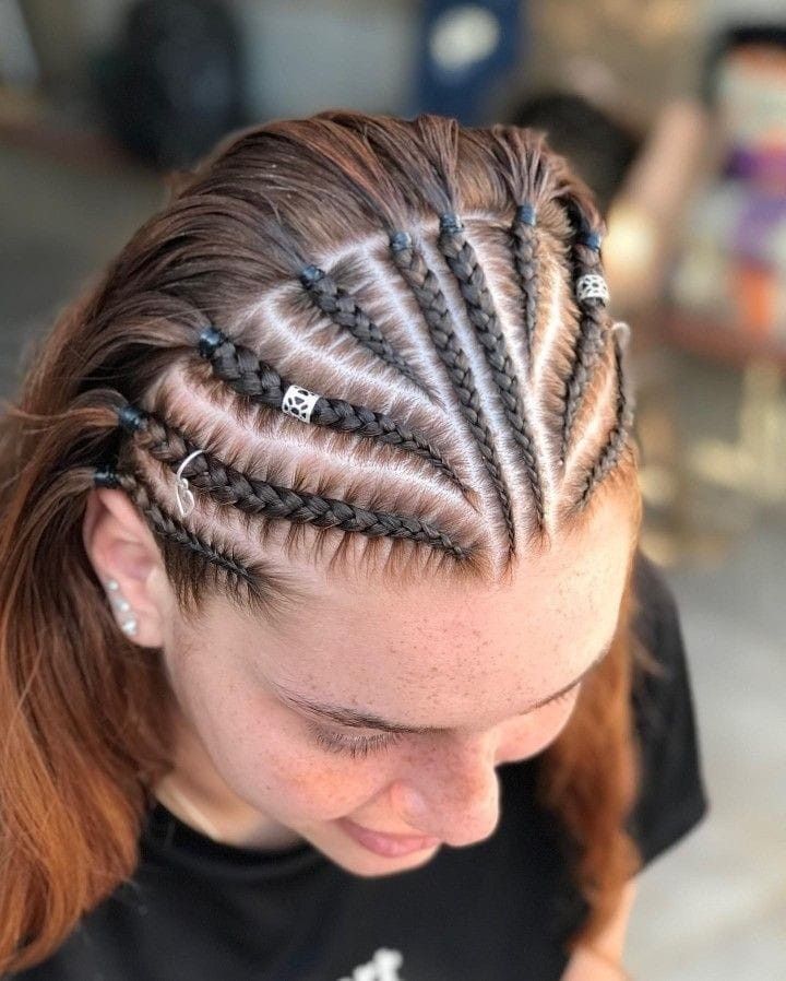 Vista superior de trenzas africanas con cuentas plateadas en una persona que mira hacia abajo y lleva una camisa negra.