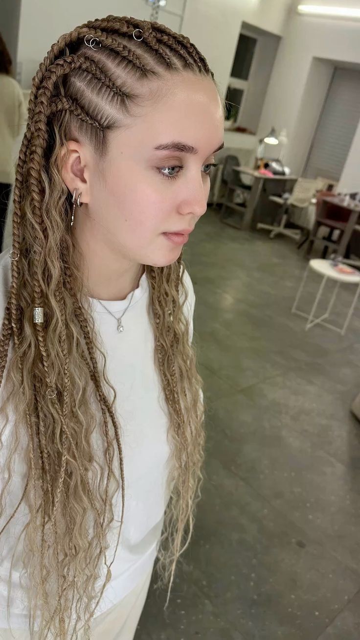 Persona con el pelo trenzado y una blusa blanca de pie en el interior de una habitación moderna.