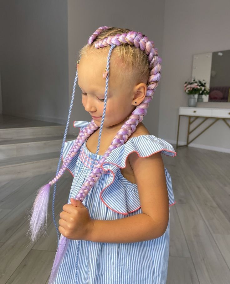 Niña pequeña con el pelo rosa trenzado, sosteniendo una trenza, vestida con un vestido de rayas azules