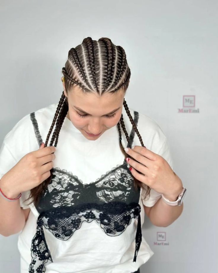 Persona con el pelo trenzado mirando hacia abajo y sujetando dos trenzas, vestida con una camisa blanca