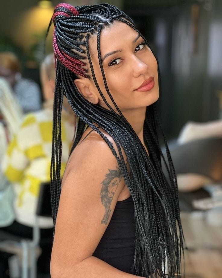 Mujer con cabello largo trenzado y un tatuaje en el hombro posando en interiores, mirando por encima del hombro.