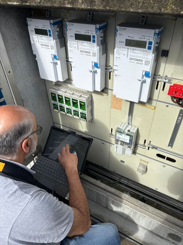 Mann verwendet Laptop zur Wartung von Stromzählern, die auf einem Außenpanel montiert sind.