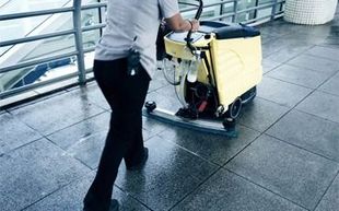 Una persona está limpiando un piso de baldosas con una máquina.