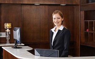 Una mujer con traje está parada en un mostrador frente a una computadora.